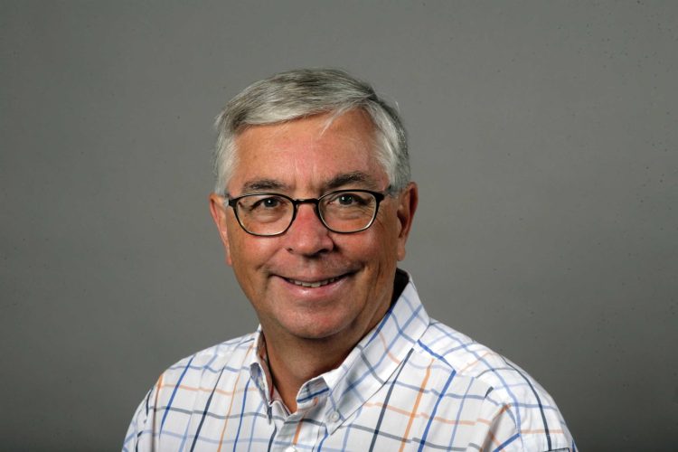 A gray-haired man with glasses smiling.